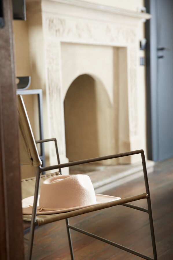 A room with a chair and a hat, a fireplace, and a door.