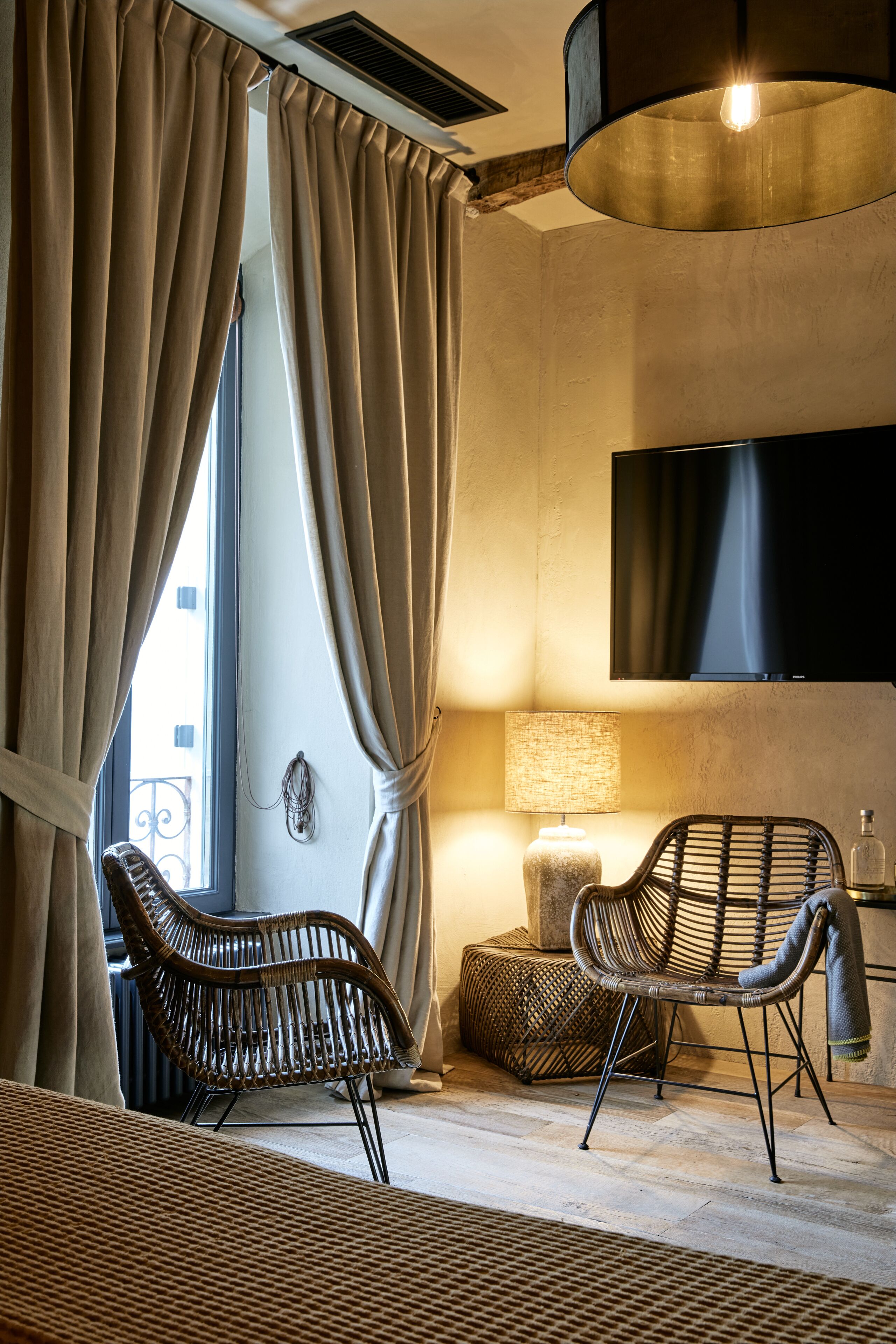 Une pièce dotée d’une grande fenêtre, de deux fauteuils en osier, d’un téléviseur à écran plat et d’une lampe.