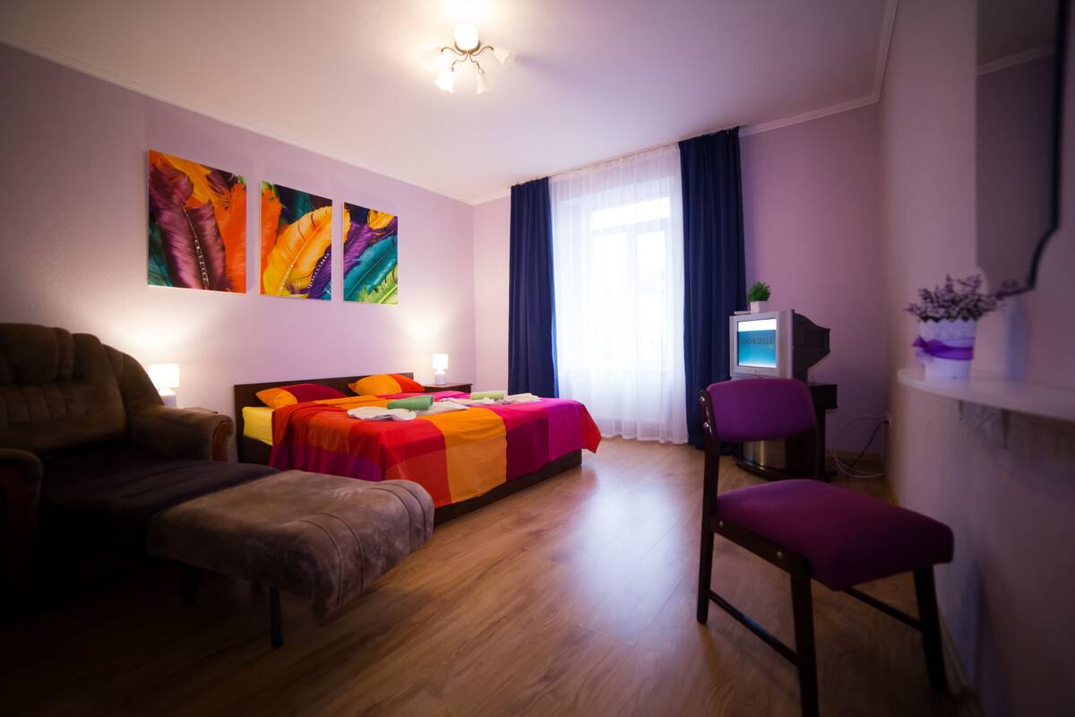 Een slaapkamer met een bed, een stoel, een bureau met een computer en kunst aan de muur.