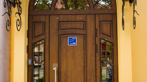 Een grote houten deur met een bord, een glazen raam en een metalen hek.