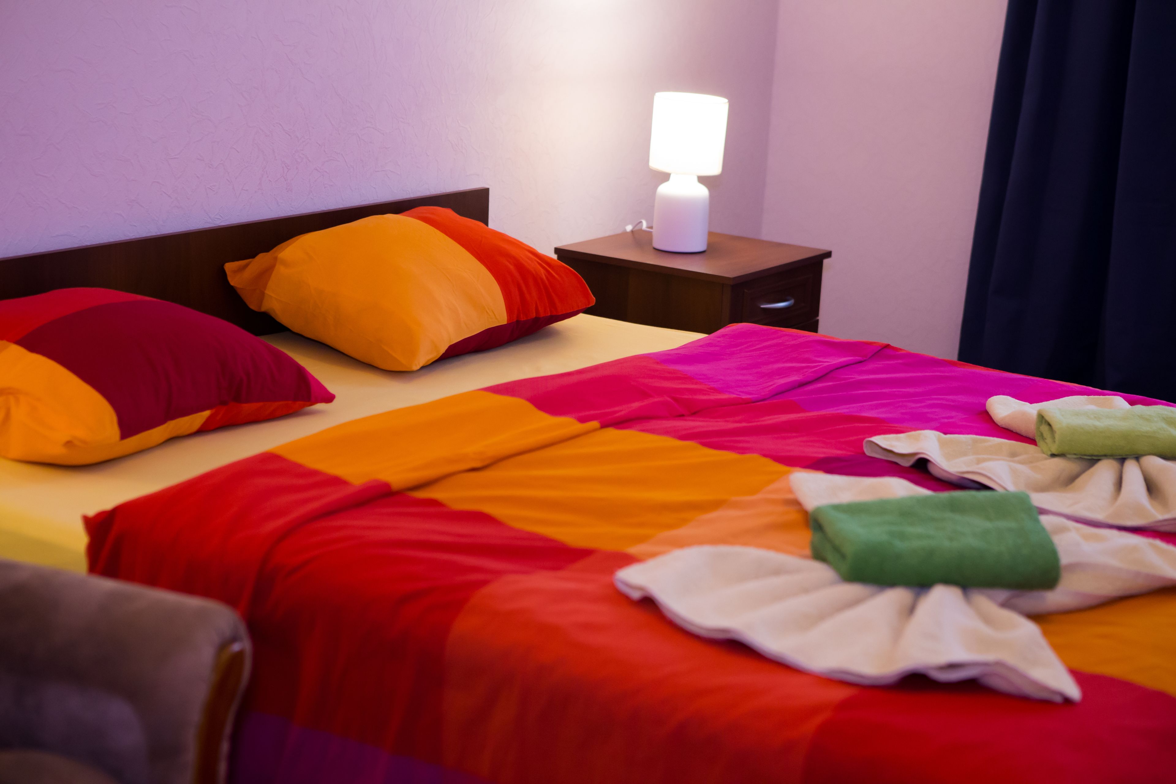 A hotel room with a neatly made bed, a bedside lamp, and a nightstand.