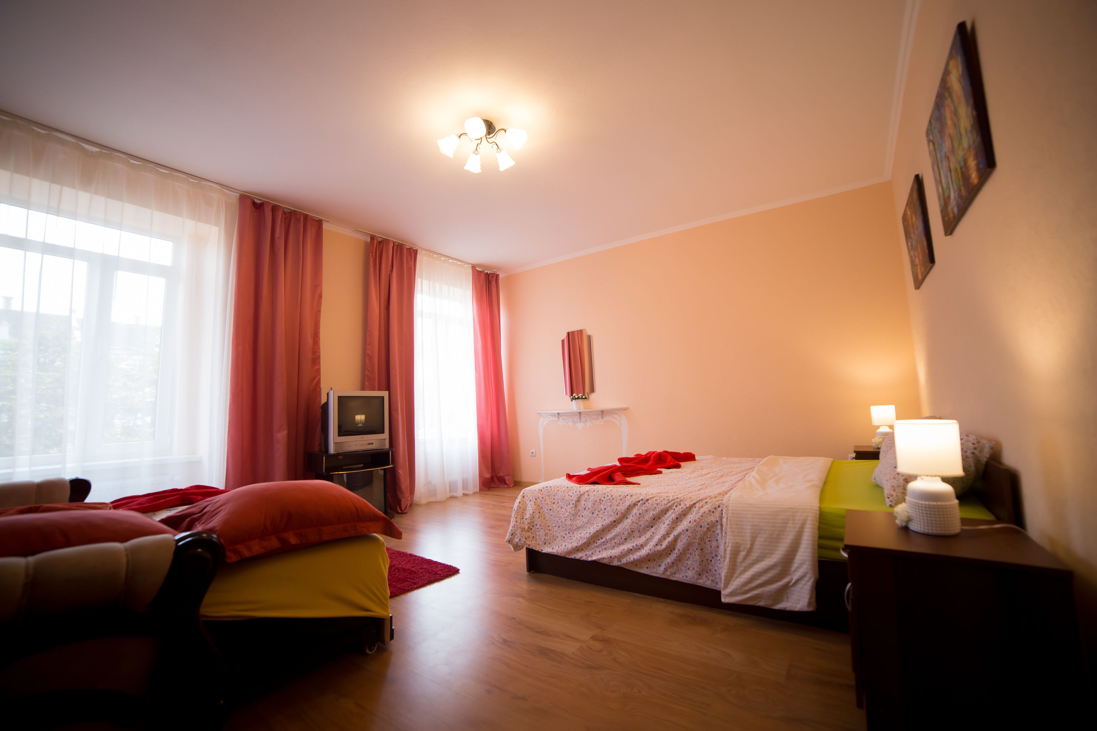 A hotel room with a bed, a TV, a desk, and a window with curtains.