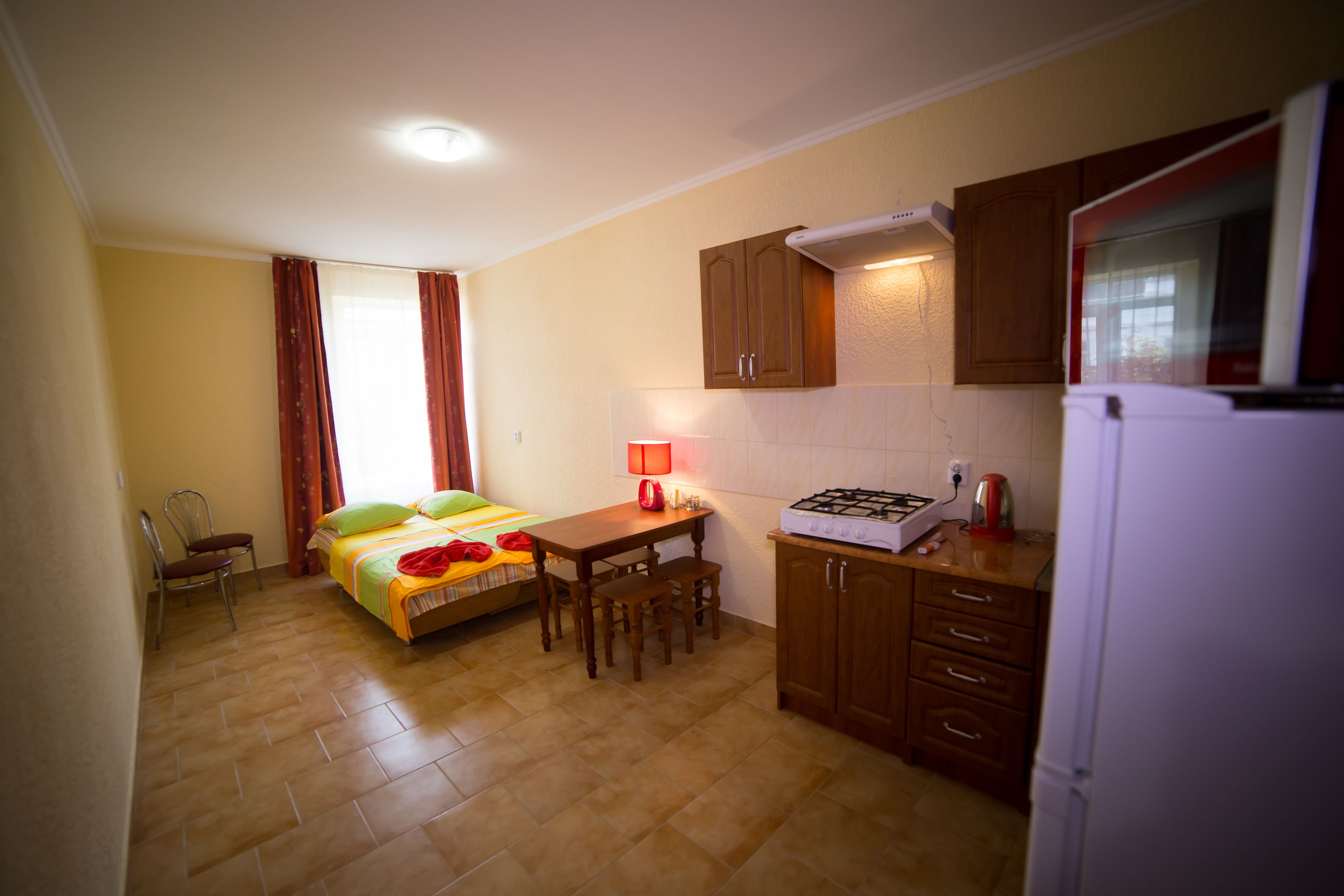 A compact kitchen with a bed, a dining table, and a refrigerator.
