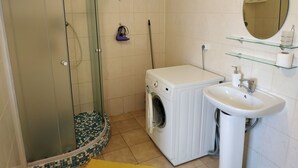 A bathroom with a glass shower enclosure, a washing machine, a sink, and a mirror.