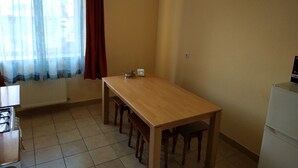 A dining area with a wooden table and benches, a window with sheer curtains, and a white refrigerator. - VIP Apartments in the Centre (Mukachevo)