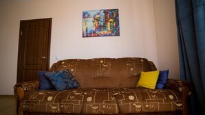 A brown sofa with a geometric pattern, two pillows (one blue, one yellow), and a colorful painting on the wall. - Best Apartments on Beregovskaya (Mukachevo)