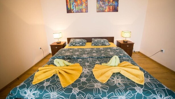 A neatly made bed with a floral bedspread, two bedside lamps, and two paintings on the wall. - Best Apartments on Beregovskaya (Mukachevo)