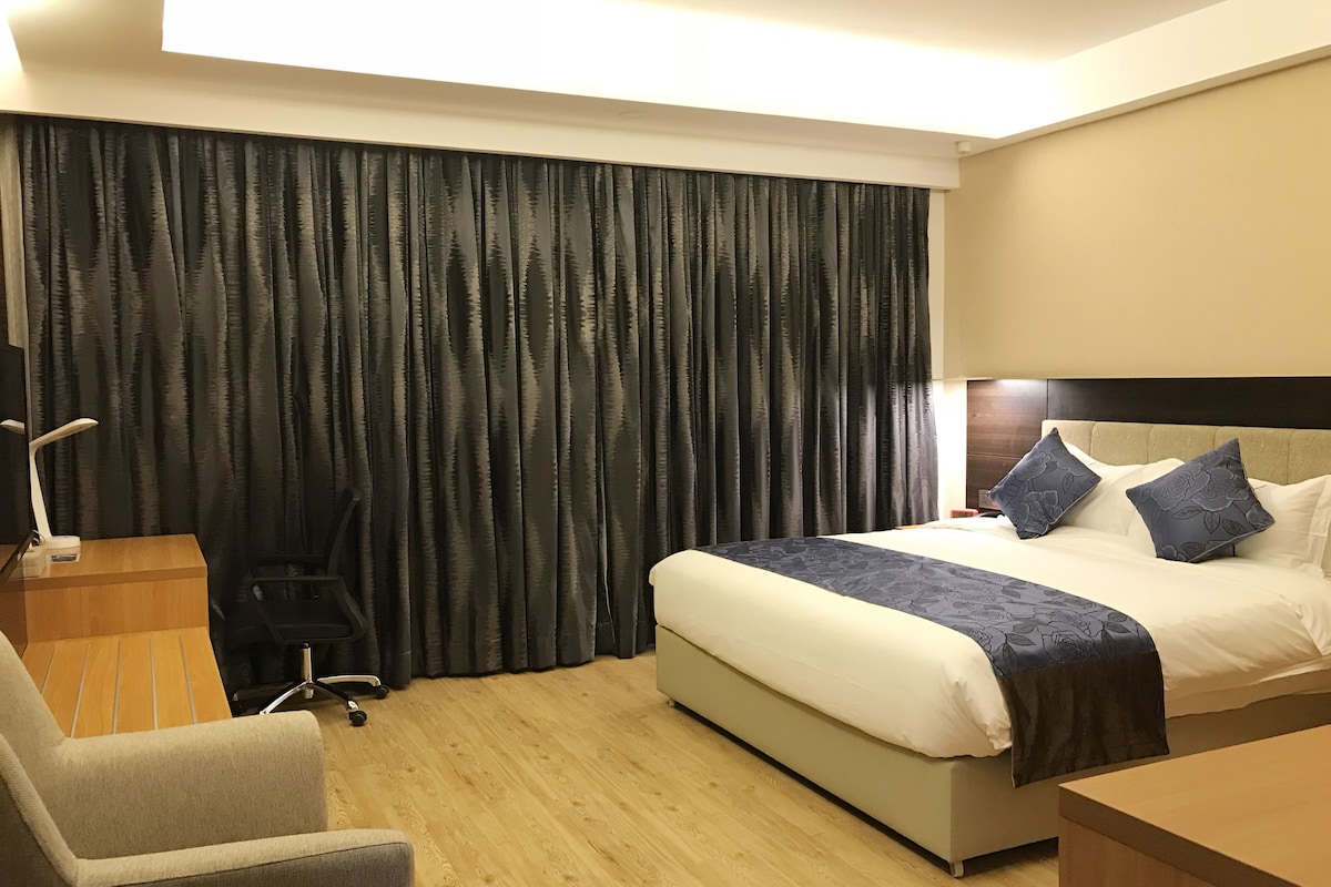 A hotel room with a bed, a desk, a chair, and a large window with curtains.