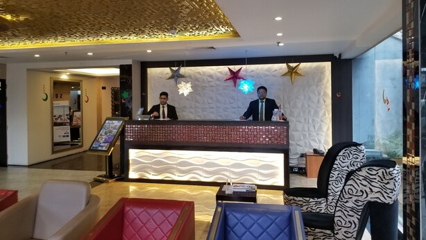 Un espace d’accueil d’hôtel au design moderne, comprenant un comptoir d’accueil, deux réceptionnistes et un coin salon avec des fauteuils confortables.