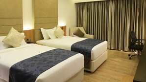 Une chambre d’hôtel avec deux lits, un bureau, une chaise et une grande fenêtre avec des rideaux.