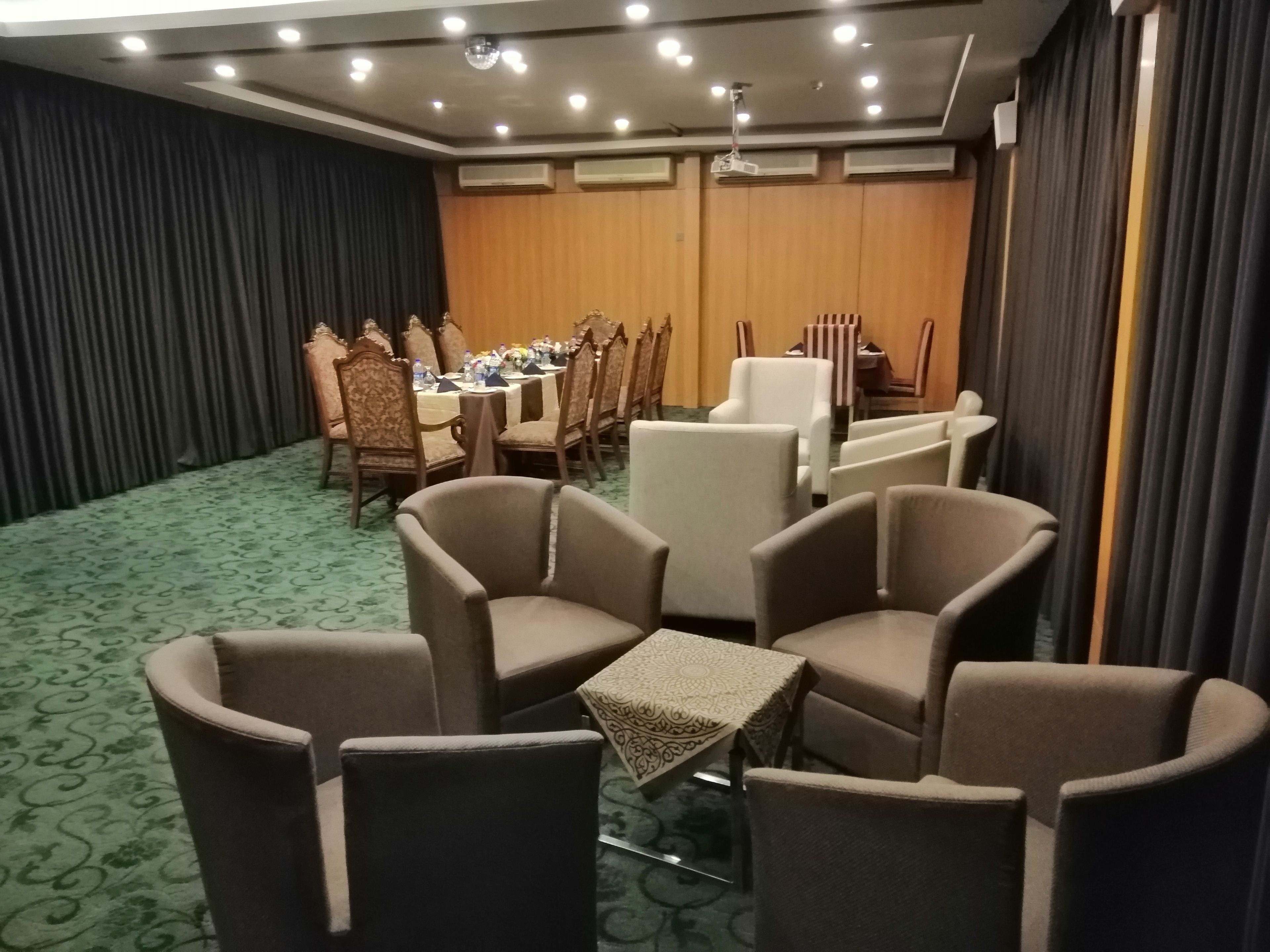 Une salle de conférence avec une longue table, de nombreuses chaises et une petite table recouverte d’une nappe à motifs.