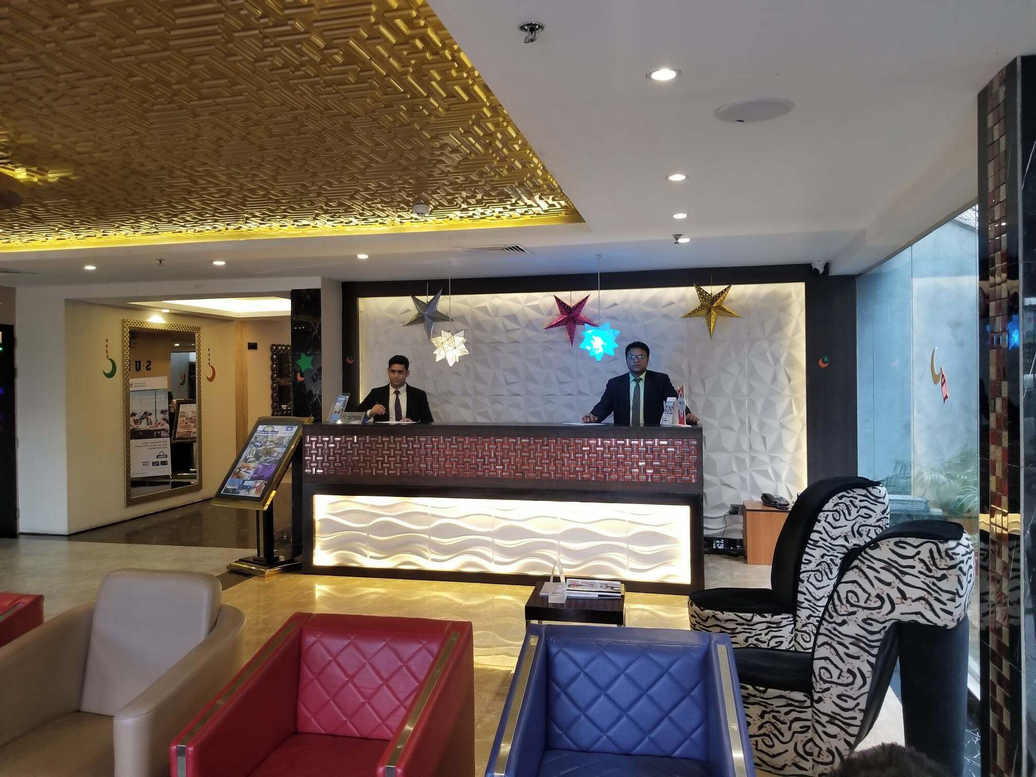 Un espace d’accueil d’hôtel au design moderne, comprenant un comptoir d’accueil, un espace salon et des éléments décoratifs.