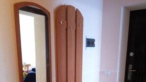 A wooden wardrobe with a mirror above it, a dark door to the right, and a tiled floor.