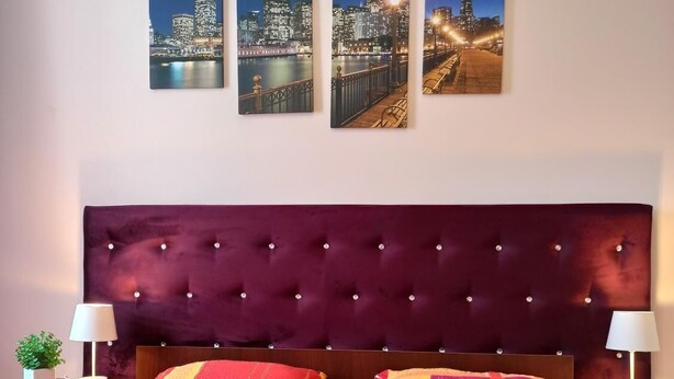 A hotel room with a large bed, a dark headboard, and three cityscape paintings on the wall.
