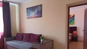 A living room with a sofa, a painting on the wall, and a door leading to another room.