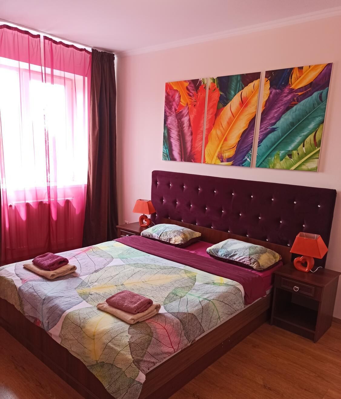 A bedroom with a large bed, a headboard, two bedside tables with lamps, and a window with curtains.