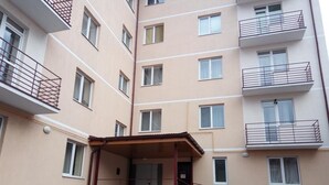 A multi-story residential building with balconies, a covered entrance, and a staircase leading to the entrance.