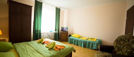 A bedroom with a large bed, a smaller bed, a chair, a TV, and a desk with a lamp.