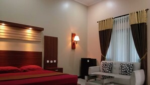 A hotel room with a bed, a sofa, a small table, a lamp, and curtains. - Rivana Hotel (Cijulang)