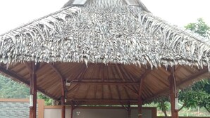 A covered outdoor seating area with a thatched roof and wooden furniture. - Rivana Hotel (Cijulang)