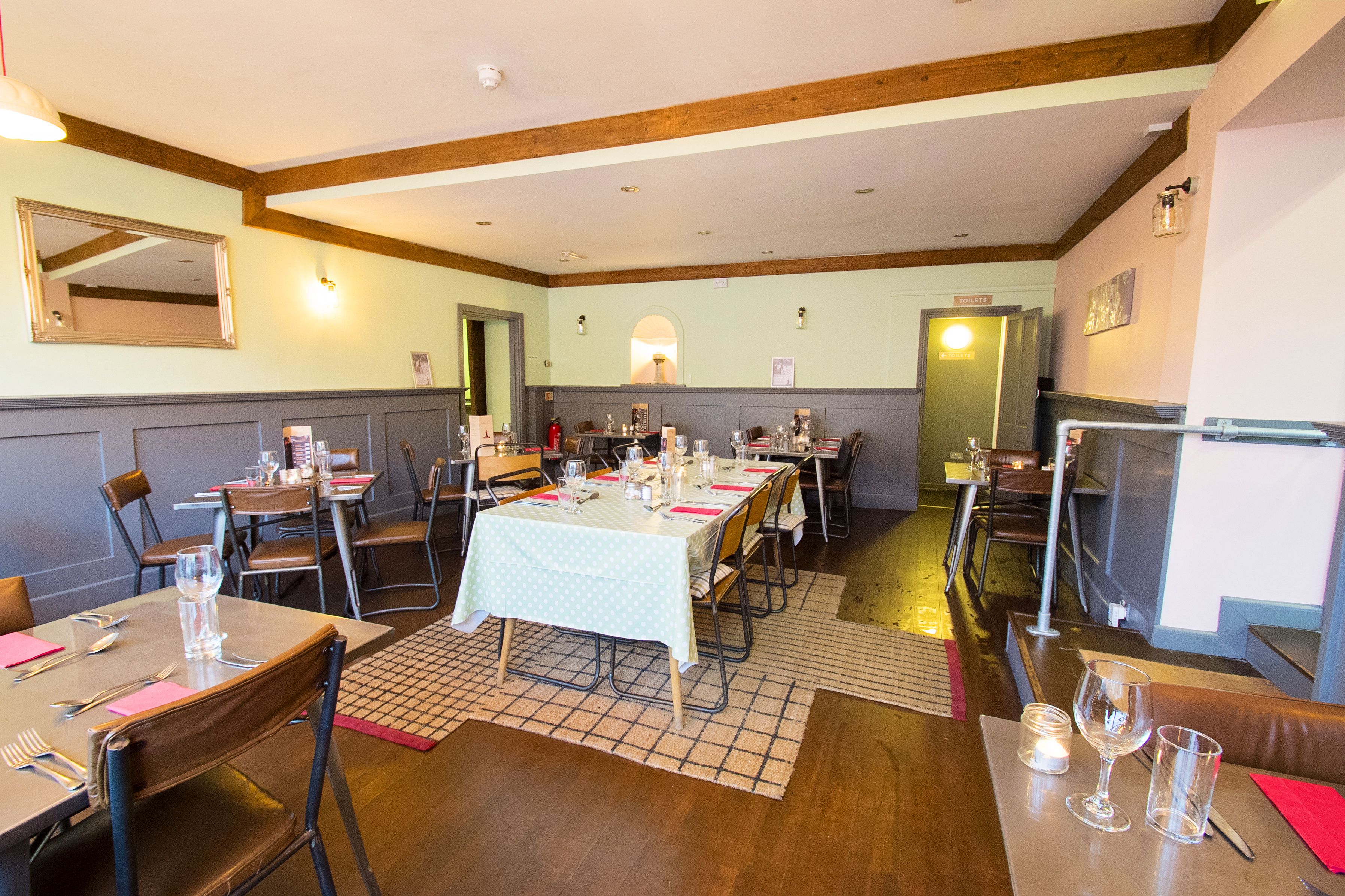 A dining area with tables set for a meal, wooden beams on the ceiling, and a mirror on the wall.