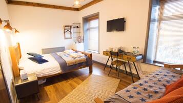 Ein Schlafzimmer mit Bett, Schreibtisch, Stuhl, Fernseher und einem Fenster mit Jalousien.