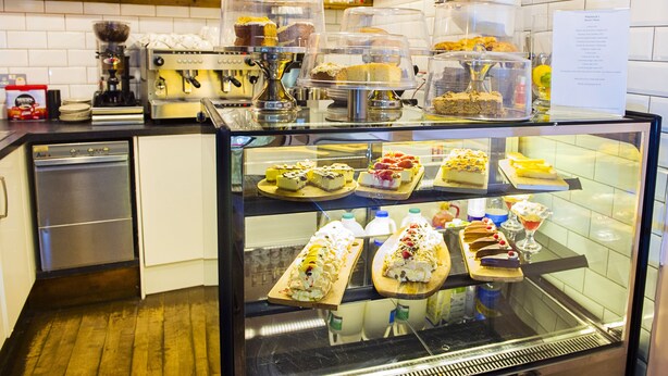 A bakery display case with various desserts. - Nik The Greek (Burry Port)