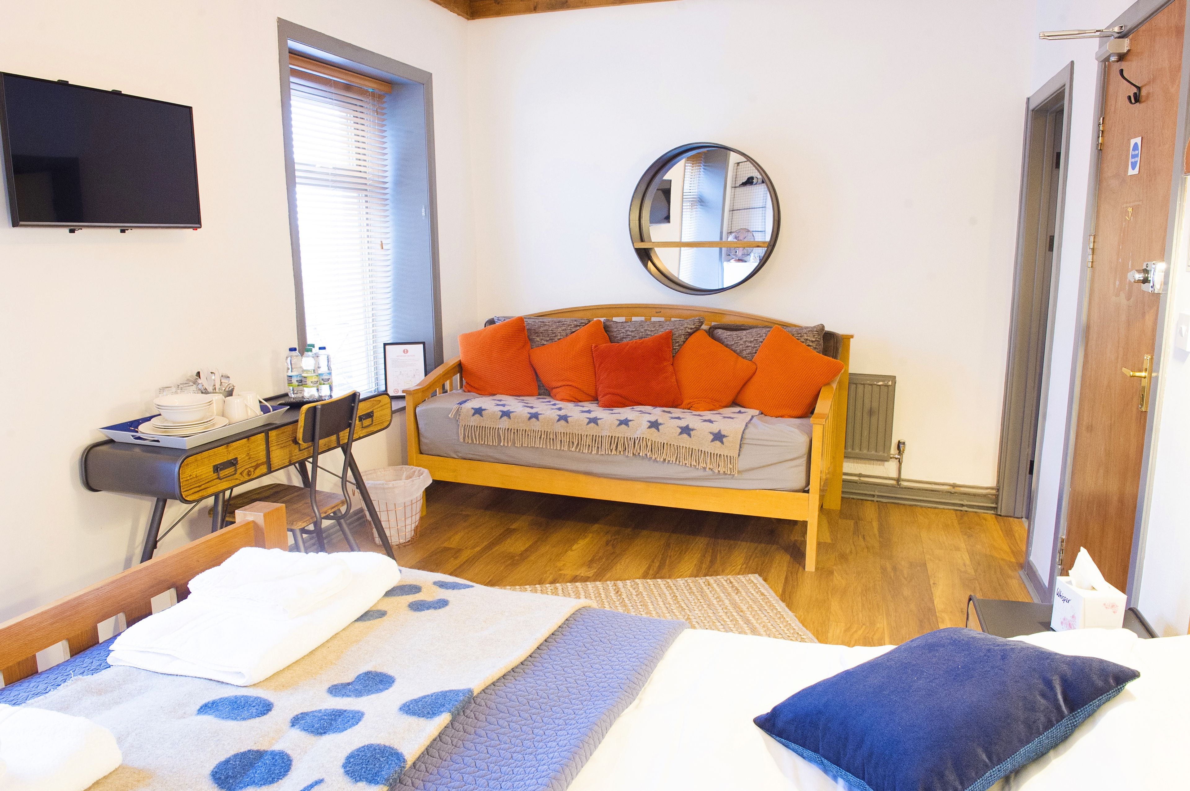 Quarto com cama, escrivaninha com cadeira, espelho e janela com persianas.