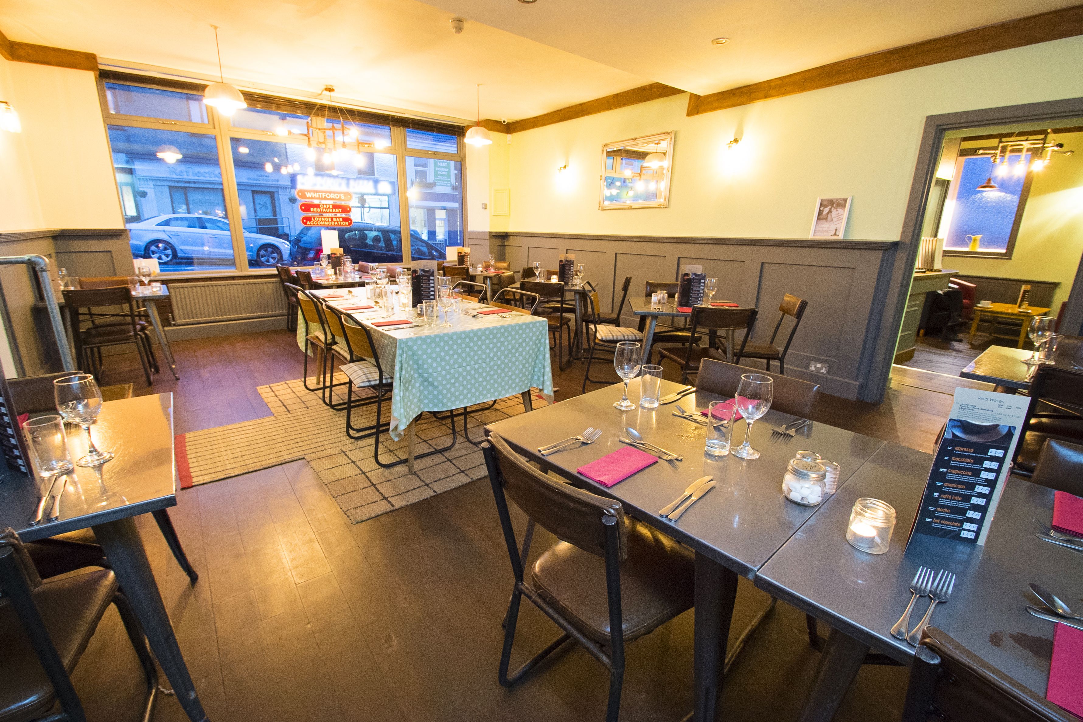 A restaurant with tables set for dining, chairs, and a view of the street through large windows.