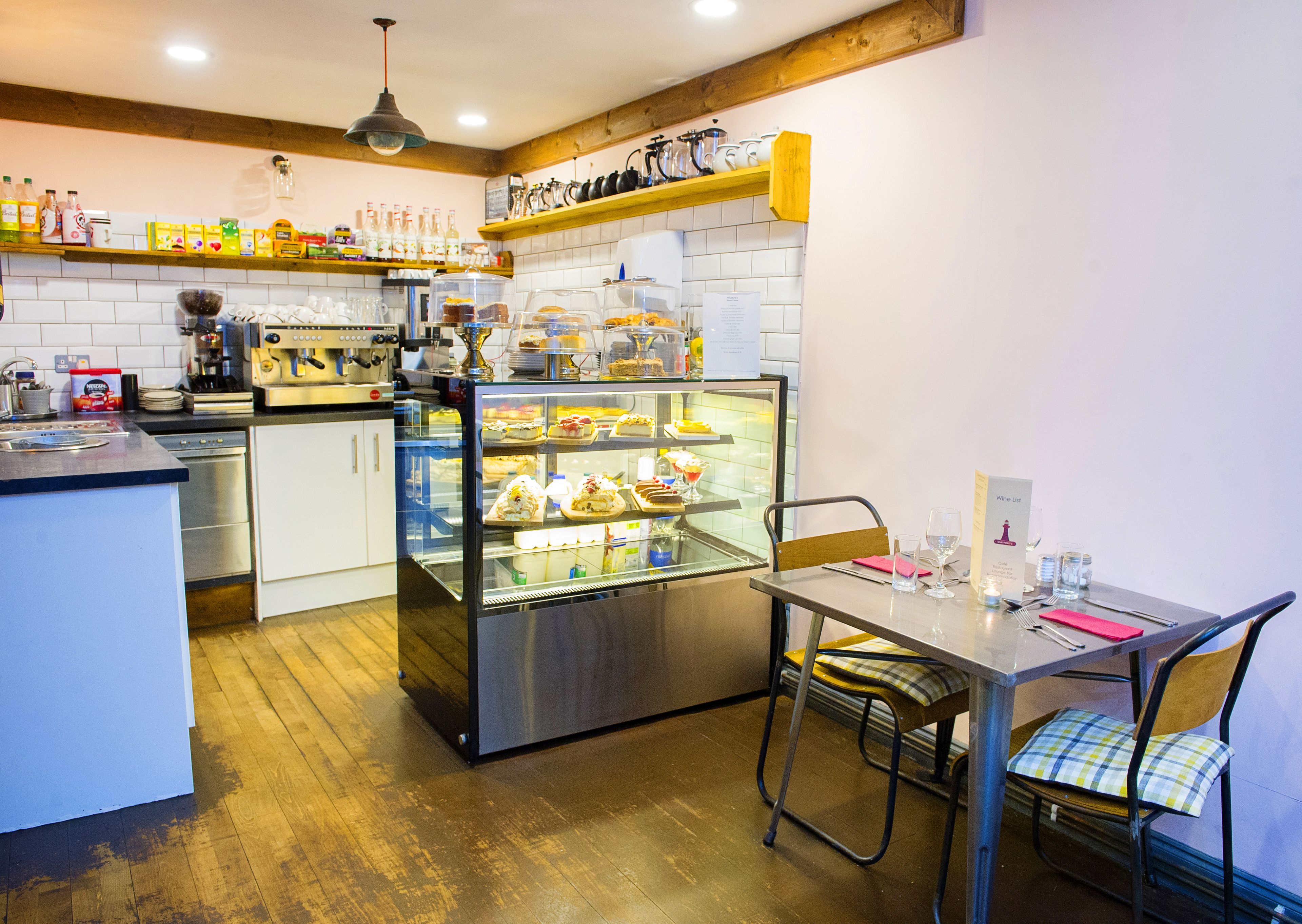 Uma cozinha com uma vitrine de sobremesas, uma máquina de café e um letreiro com a carta de vinhos.