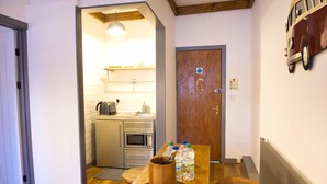 A compact kitchen with a microwave, kettle, and sink. There is a wooden table with a cup and water bottles. A door with a sign is visible in the background. - Nik The Greek (Burry Port)