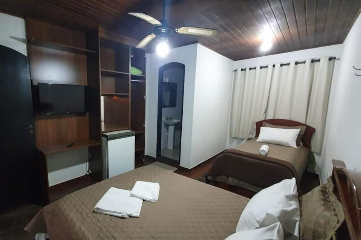 Une chambre avec un lit, un bureau, une armoire et un ventilateur de plafond.