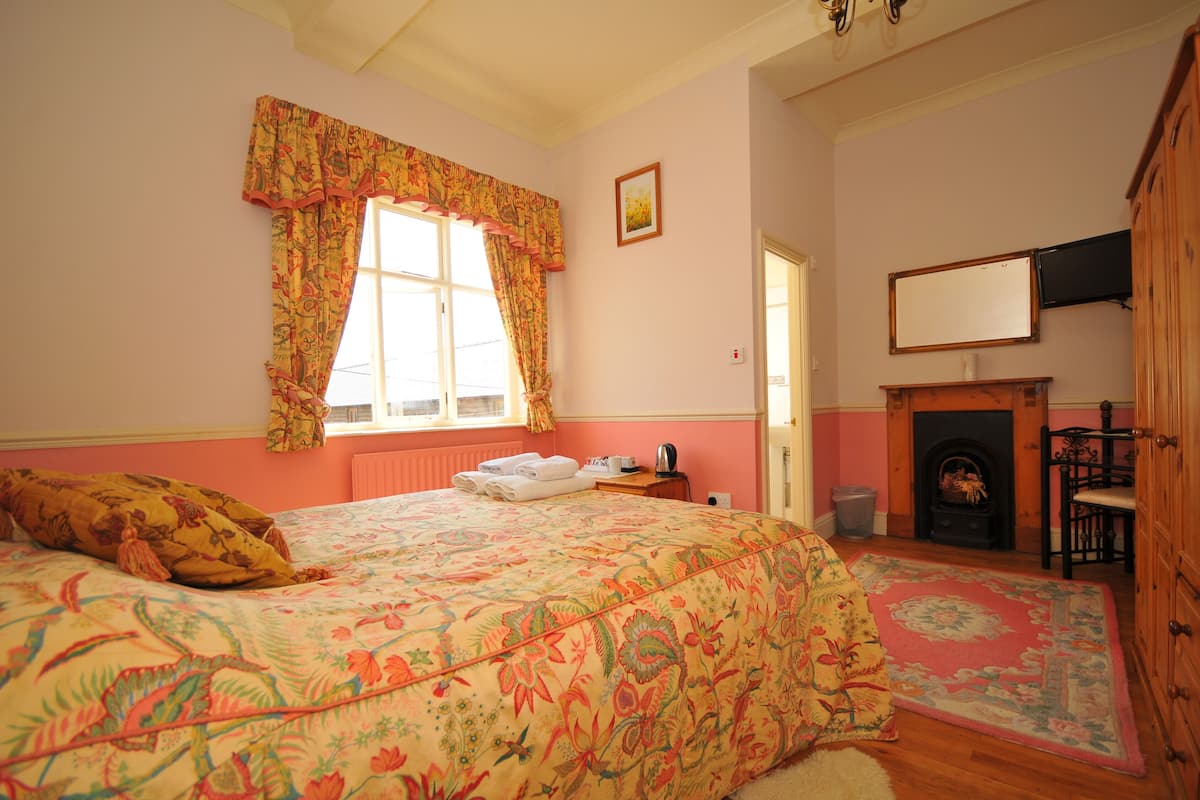 A bedroom with a large bed, a fireplace, and a window with curtains.