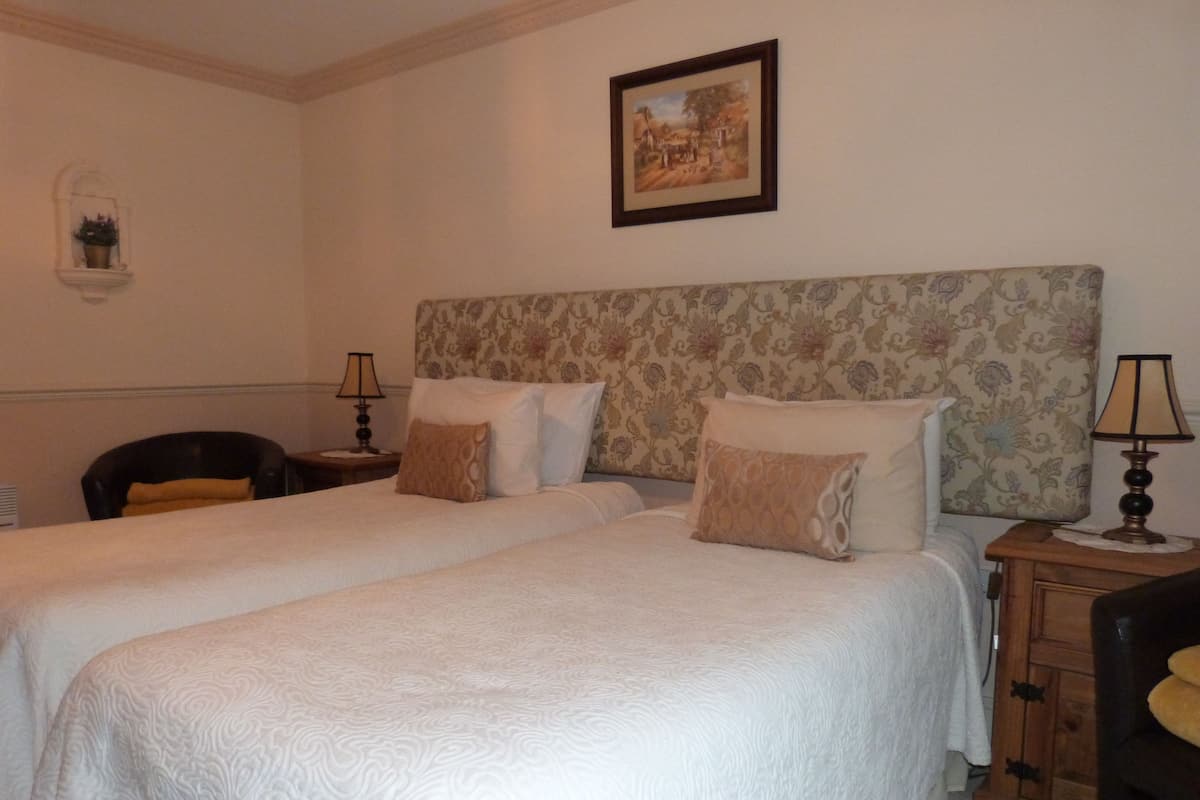 A hotel room with two beds, a nightstand with a lamp, a chair, and a framed picture on the wall.