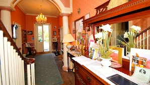 A hotel lobby with a grand staircase, a chandelier, and a reception desk with various items and a mirror. - Edderton Hall Country House (Welshpool)