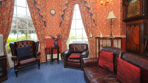 A room with a leather armchair, a sofa, a small table with a vase, and a clock on the wall. - Edderton Hall Country House (Welshpool)