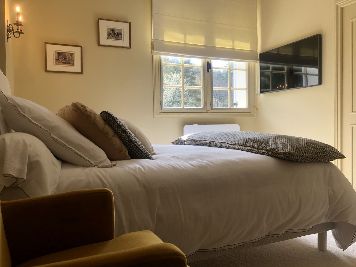 A bedroom with a bed, a chair, a window, and wall-mounted artwork.