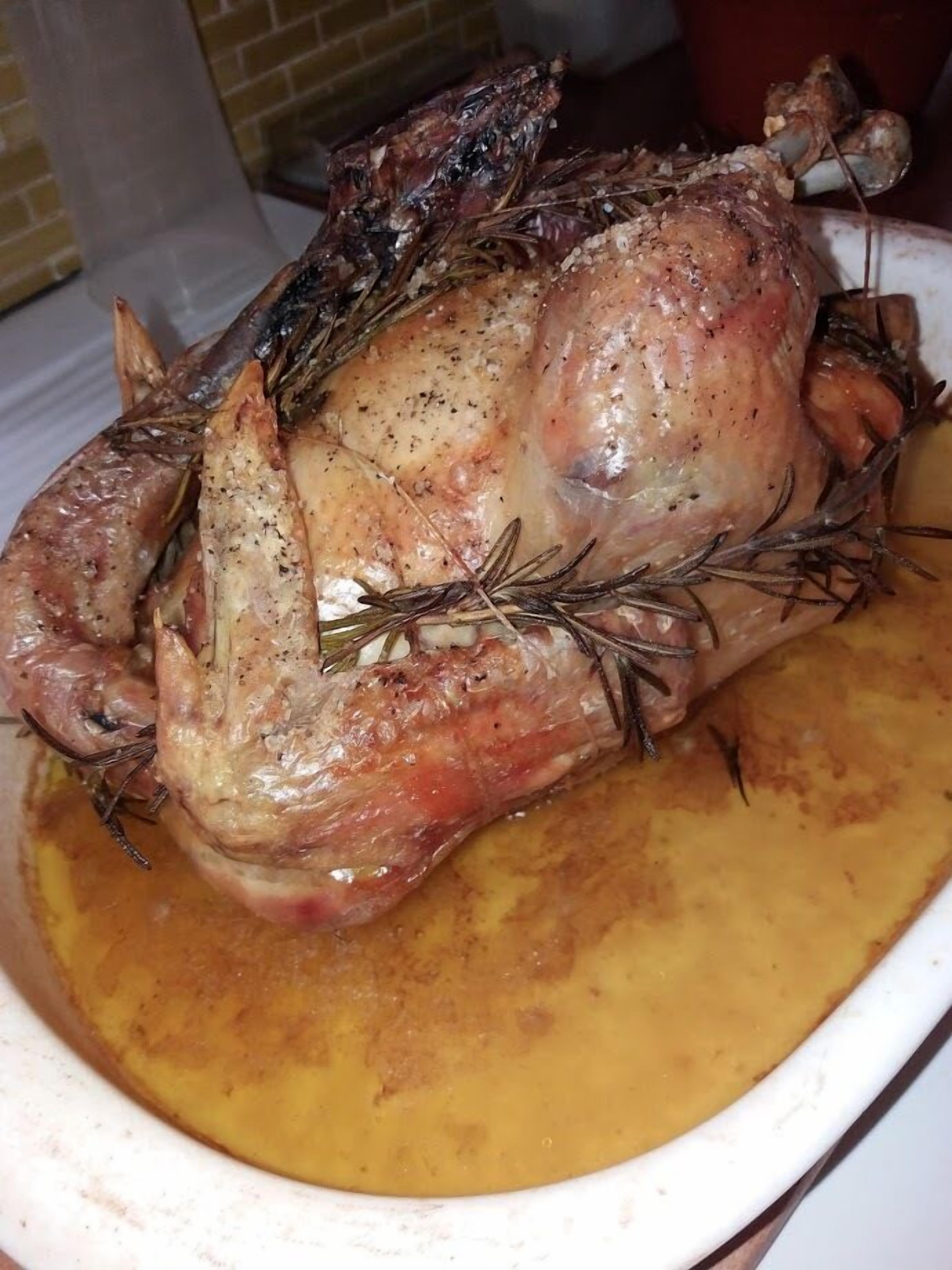 A roasted chicken in a white dish with a golden-brown sauce.