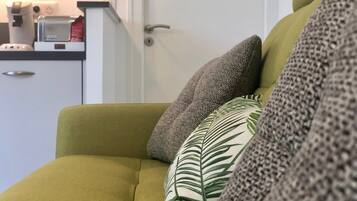 A green sofa with multiple cushions, a coffee machine, and a small cabinet in the background.