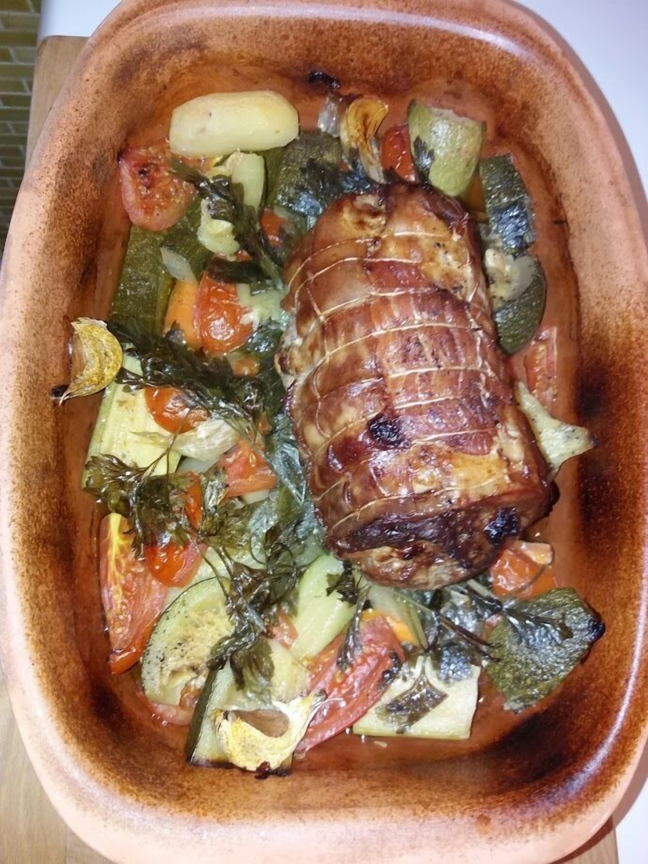 Un plat de viande rôtie accompagné de légumes, le tout présenté dans un plat de cuisson en céramique.