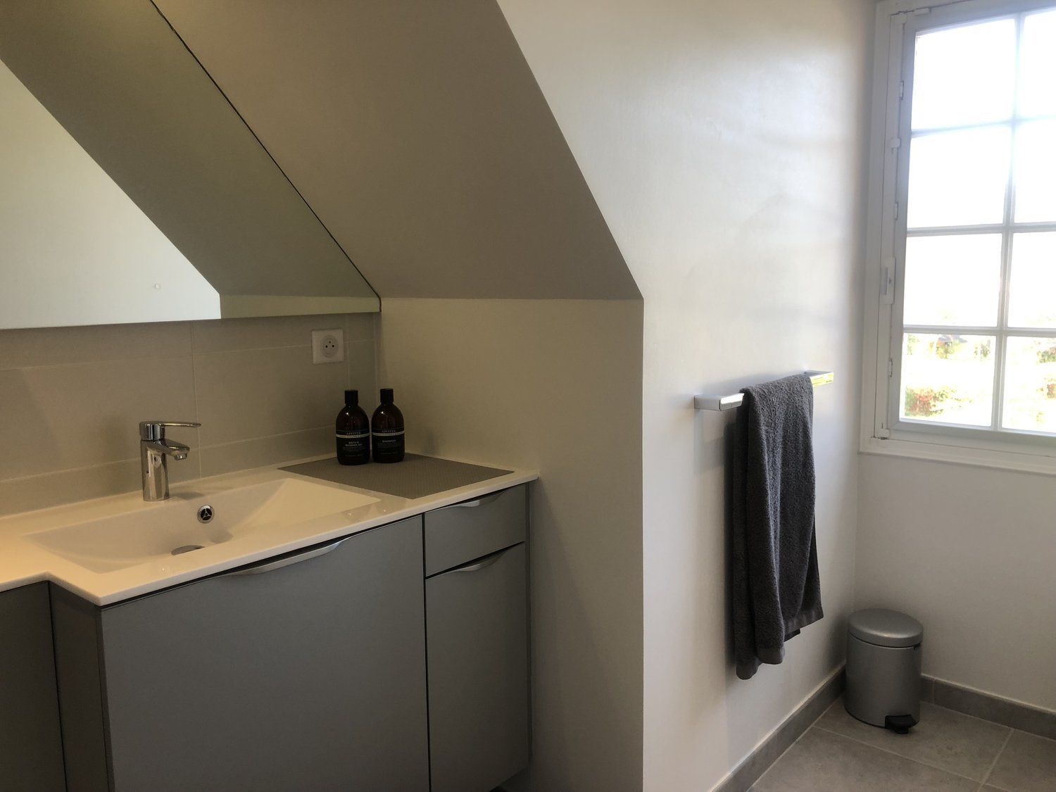A modern bathroom with a white sink, grey cabinets, a towel rack, and a window with a view.