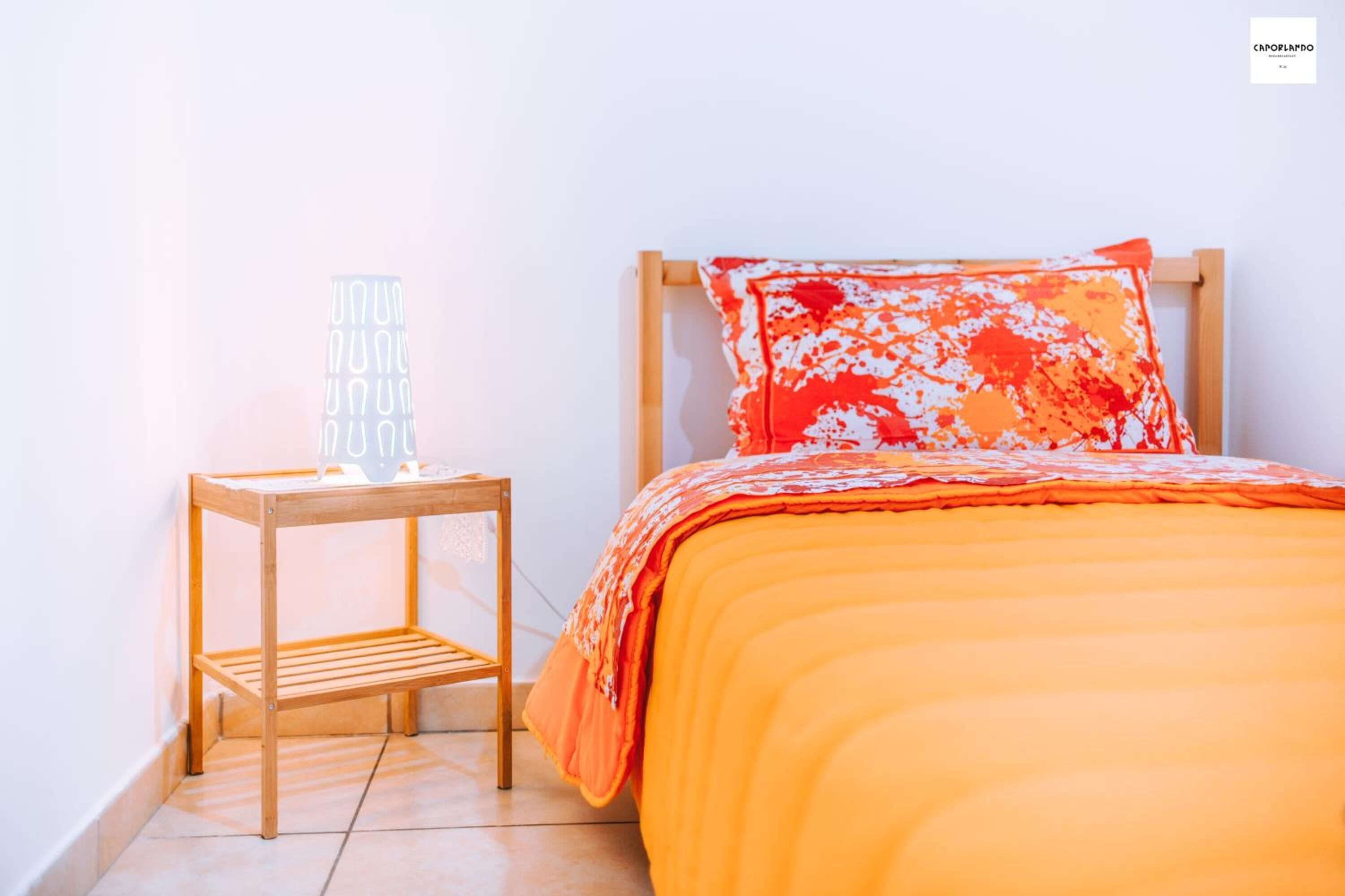 Une chambre à coucher avec un lit en bois, une couvre-lit orange et une table de chevet avec une lampe.