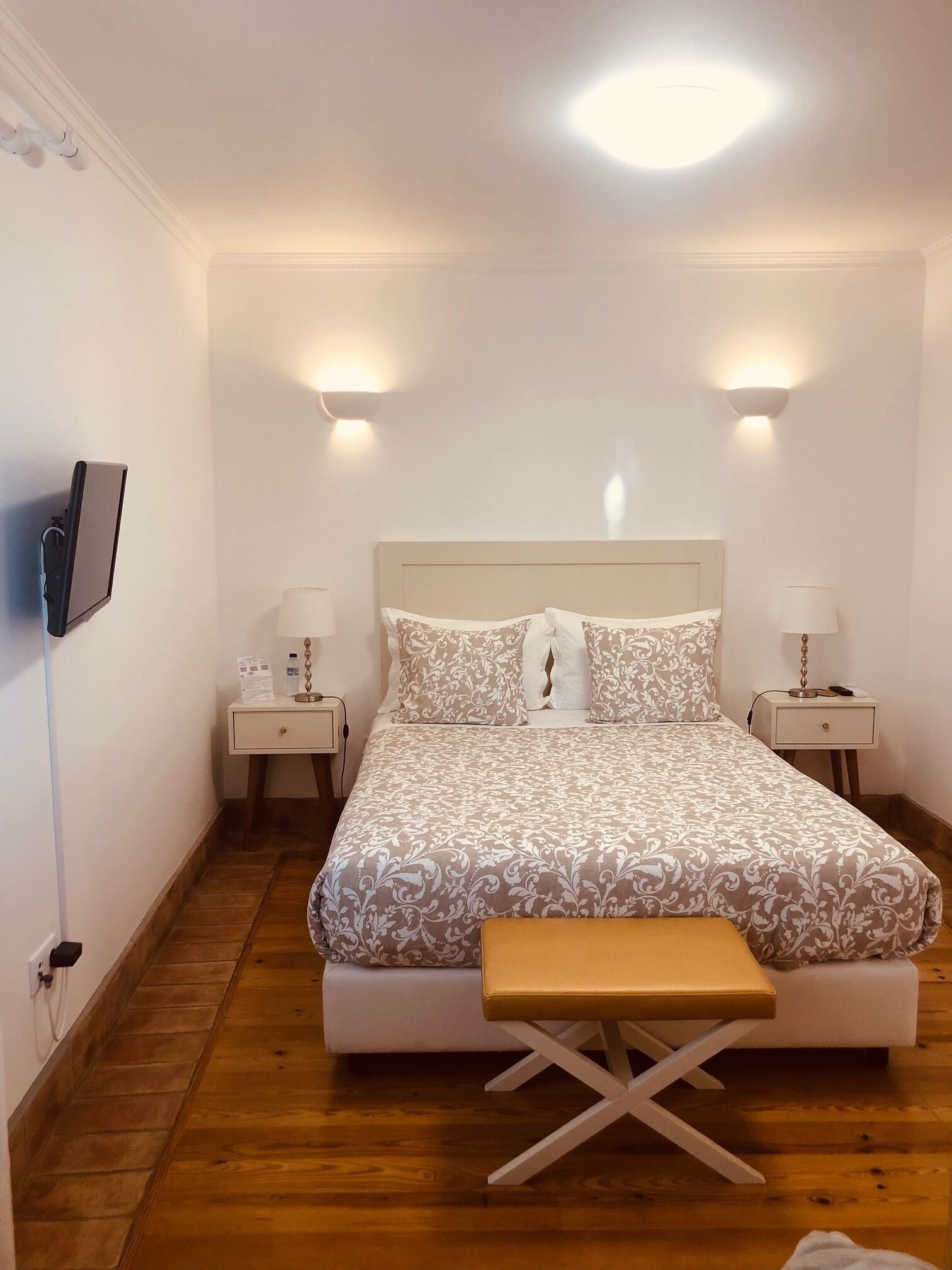 Un dormitorio con cama, mesitas de noche, televisor y un banco.