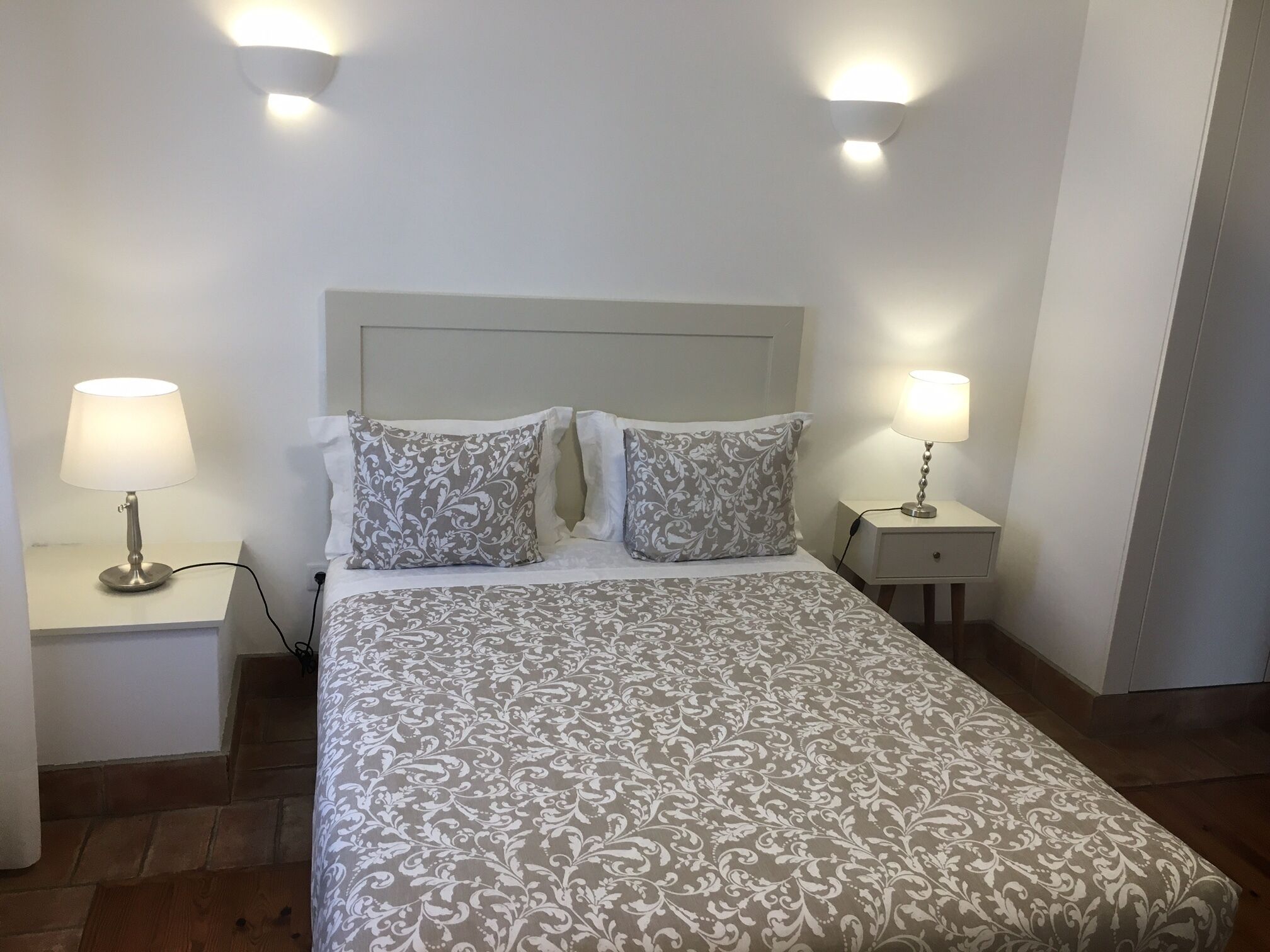A neatly made bed with patterned bedding, two bedside lamps, and a simple headboard.