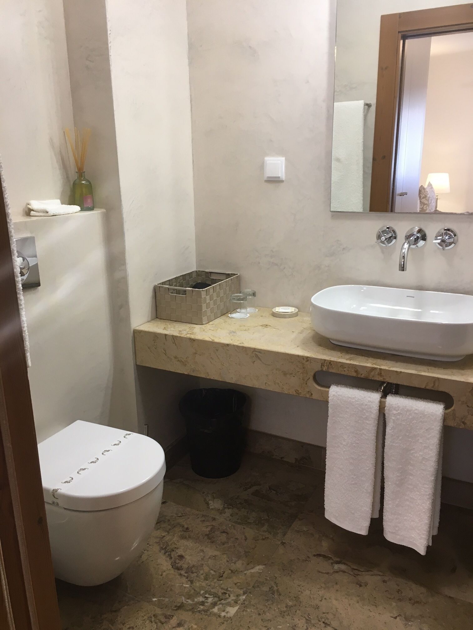 A bathroom with a white toilet, a sink with a mirror above it, and a towel rack with two towels.