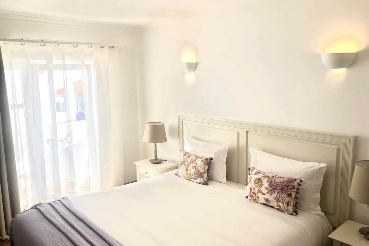 A hotel room with a large bed, two bedside lamps, and a window with curtains.
