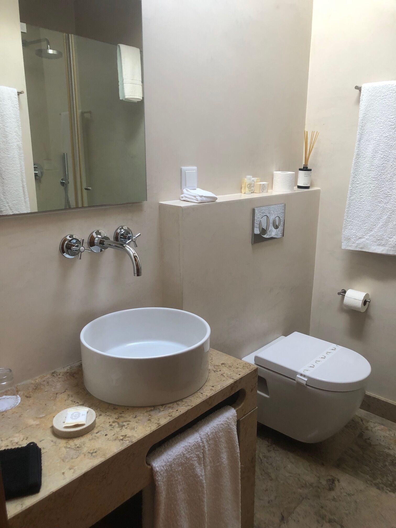 A bathroom with a large round sink, a toilet, a mirror, and a shower area.