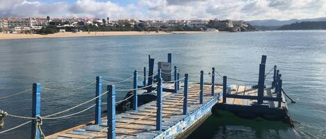 Un muelle se adentra en aguas tranquilas con un letrero que dice 'PRIVATE', con vistas a una playa y edificios a lo lejos.