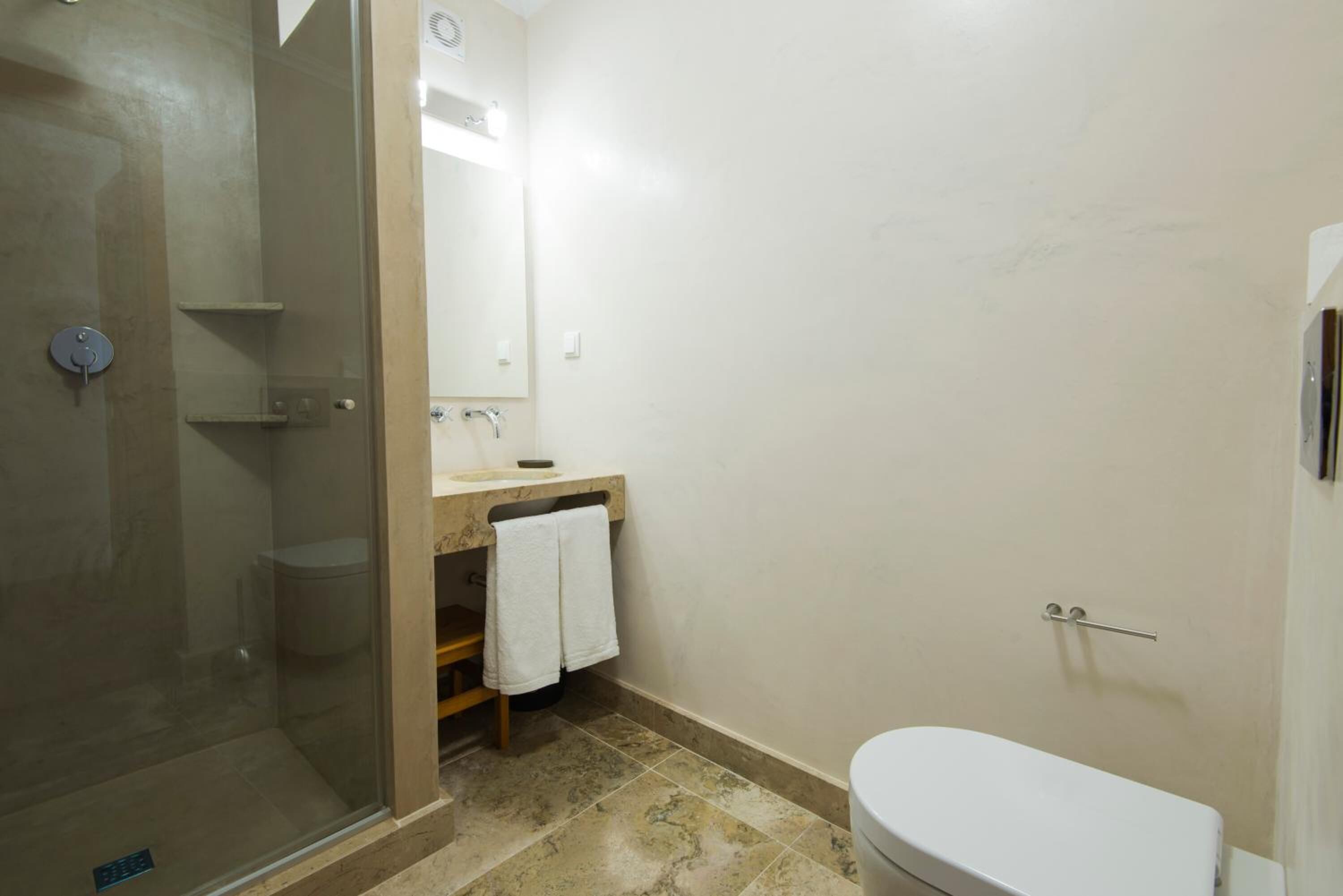 A bathroom with a glass-enclosed shower, a sink with a mirror, and a toilet.