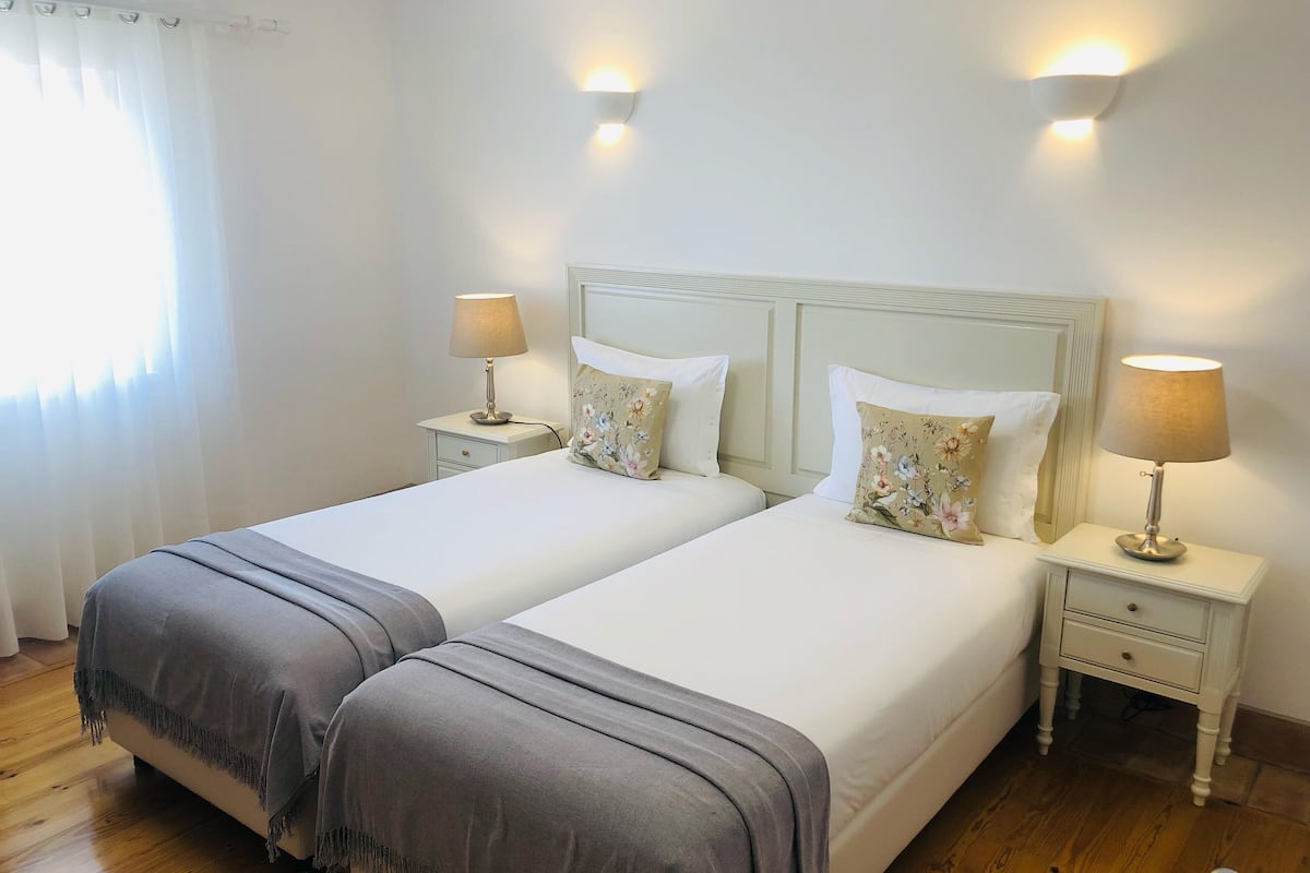 A double bed with two nightstands, each with a lamp, in a room with wooden flooring and a white headboard.